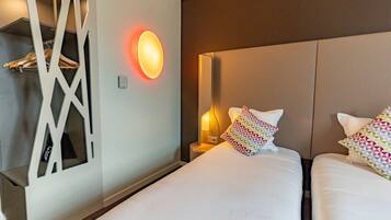 A hotel room with two beds, a wall-mounted light, and a coat rack.