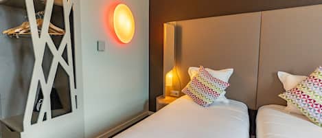 A hotel room with two beds, a wall-mounted light, and a coat rack.