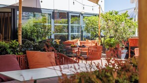 An outdoor seating area with orange chairs and tables, surrounded by greenery and a glass wall. - Campanile PRIME - Montpellier Centre St Roch (Montpellier)