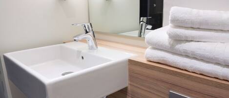 A modern bathroom with a white sink, a mirror, and a stack of white towels.