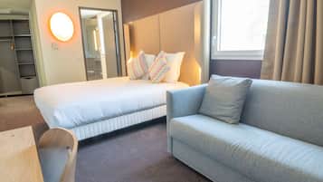 A hotel room with a bed, a sofa, a mirror, and a window with curtains.