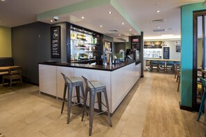 A bar area with stools, a counter, and a display of bottles. - Premier Inn Manchester Salford Media City (Salford)
