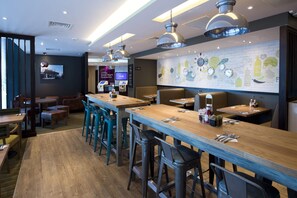 Ein Restaurant mit Holztischen und -stühlen, Pendelleuchten und einer Wand mit einer Wandmalerei zum Thema Essen.