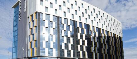 En modern byggnad med en glasfasad, flera fönster och en skylt som visar att det är hotellet ”Tomorrow Hotel”.