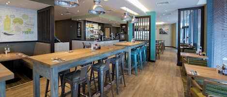 A modern restaurant with long wooden tables, bar stools, and pendant lighting.
