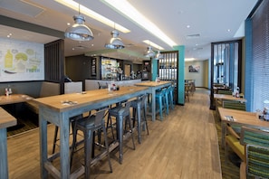 A modern restaurant with long wooden tables, bar stools, and pendant lighting.