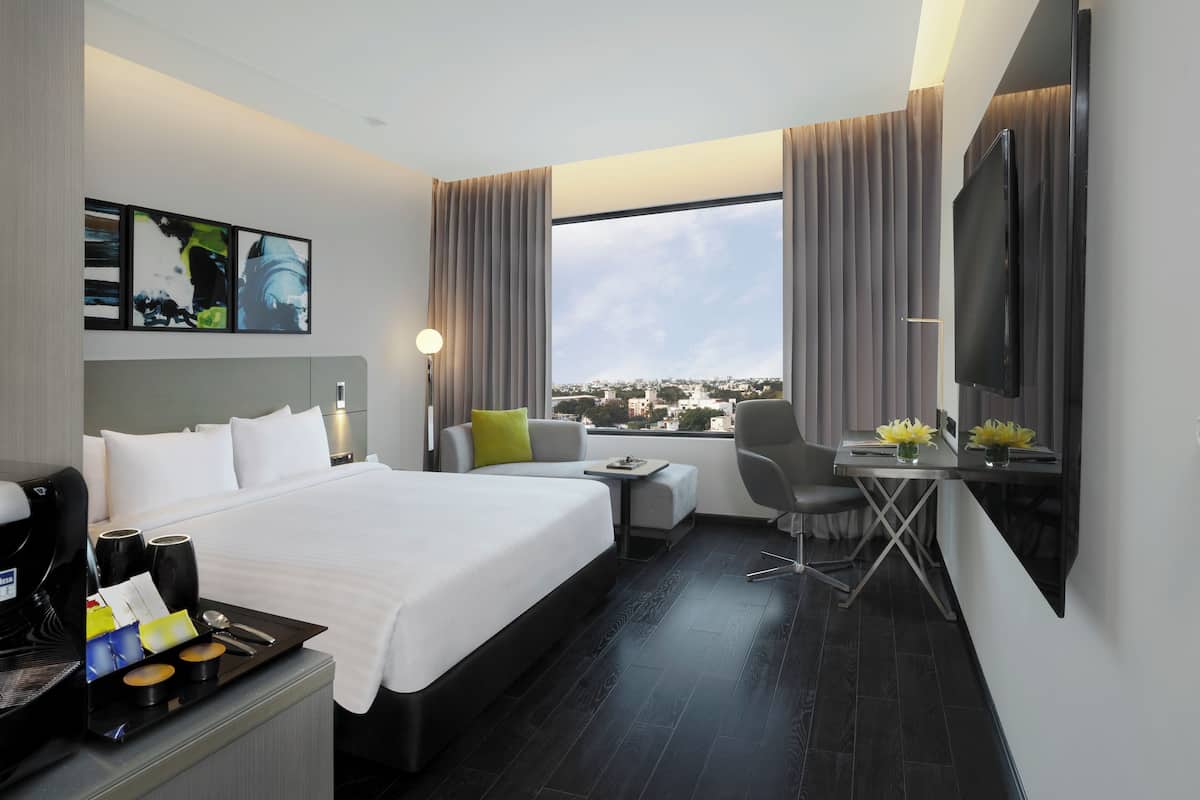 A hotel room with a bed, a desk, a chair, a TV, and a window with a city view.