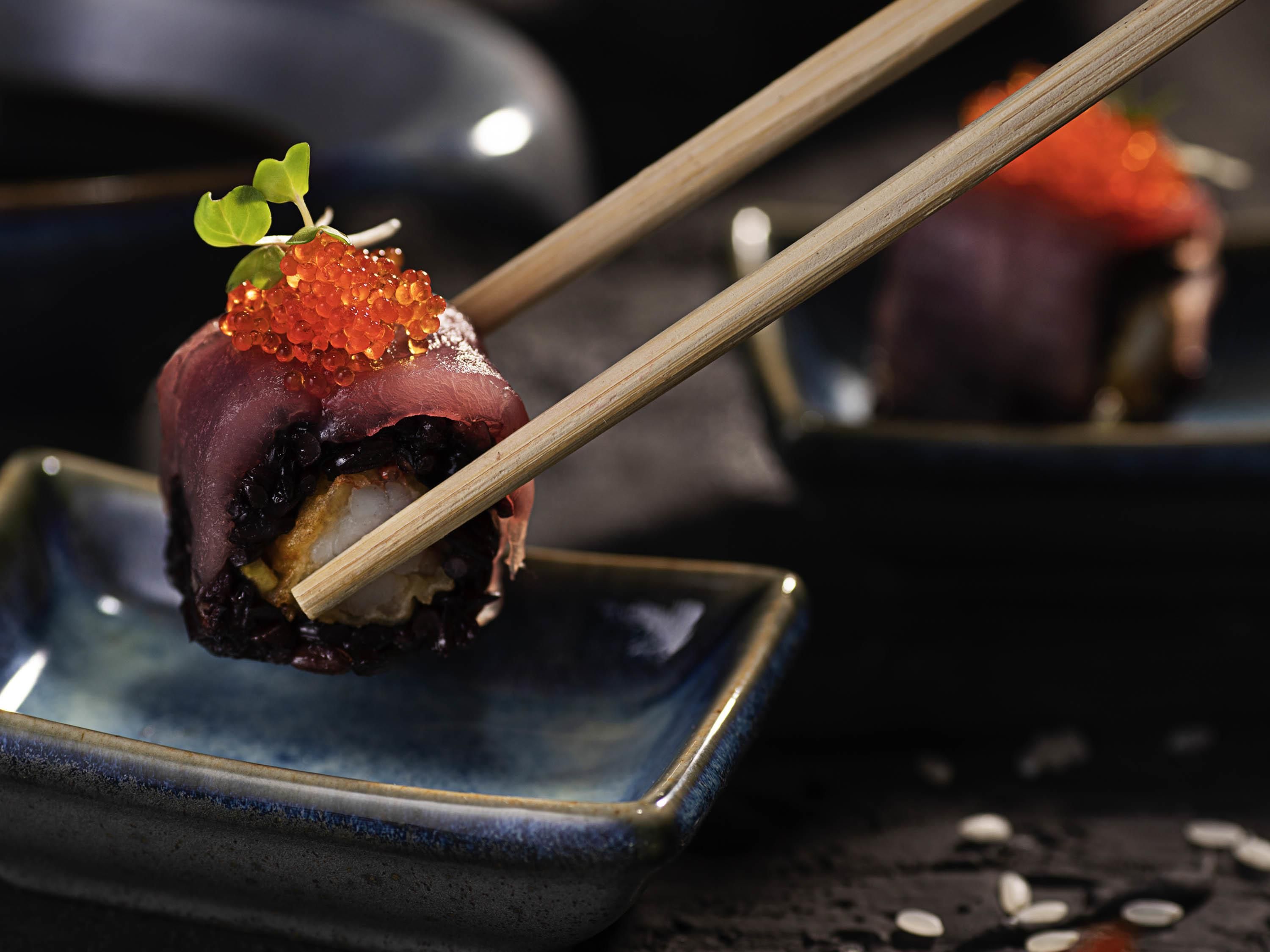 A sushi dish with chopsticks on a dark ceramic plate.