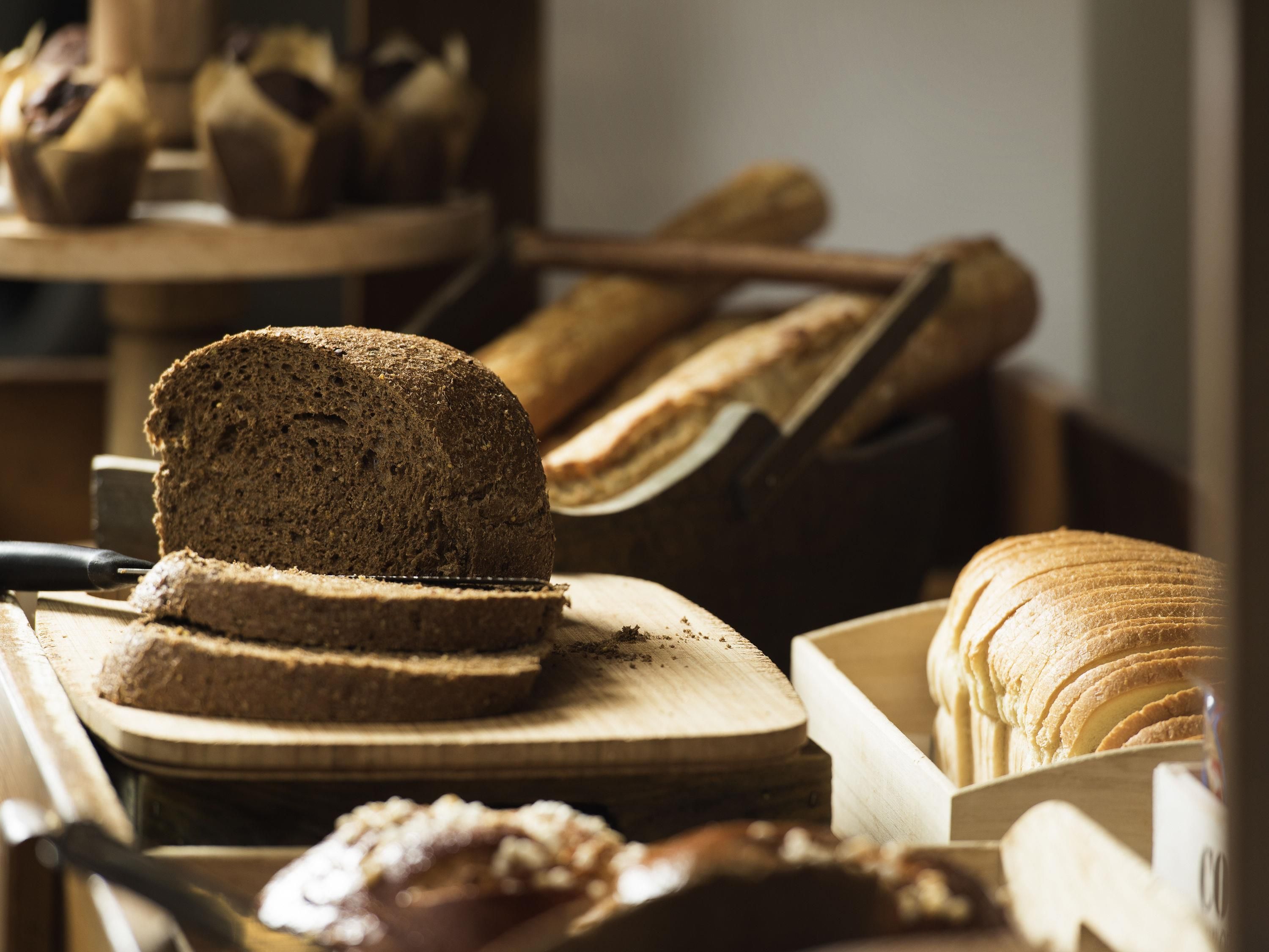 Een stuk donker brood, een stuk wit brood en een pak plakjes wit brood op een houten snijplank.