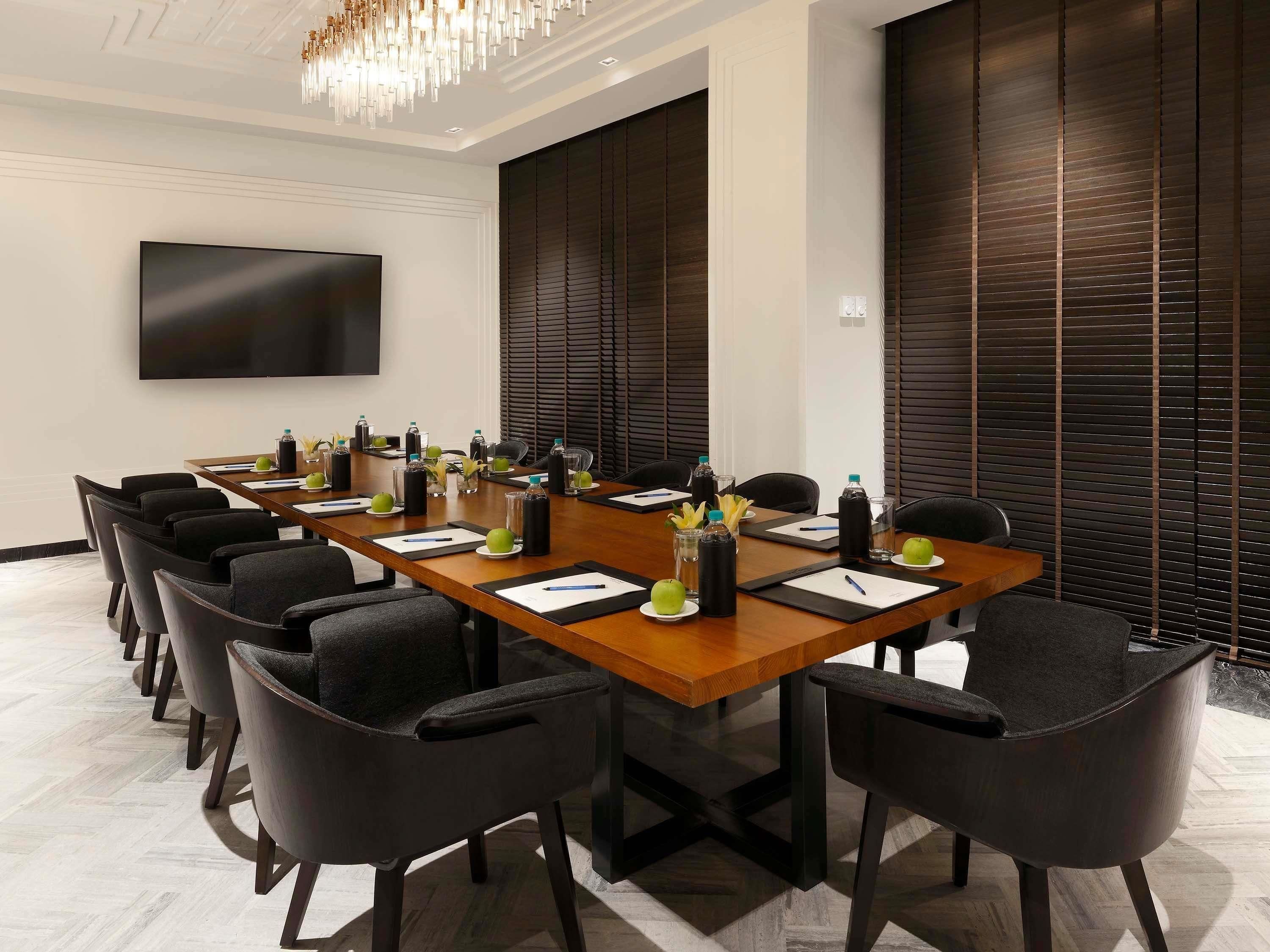 A conference room with a long table, chairs, a flat-screen TV, and a modern chandelier.