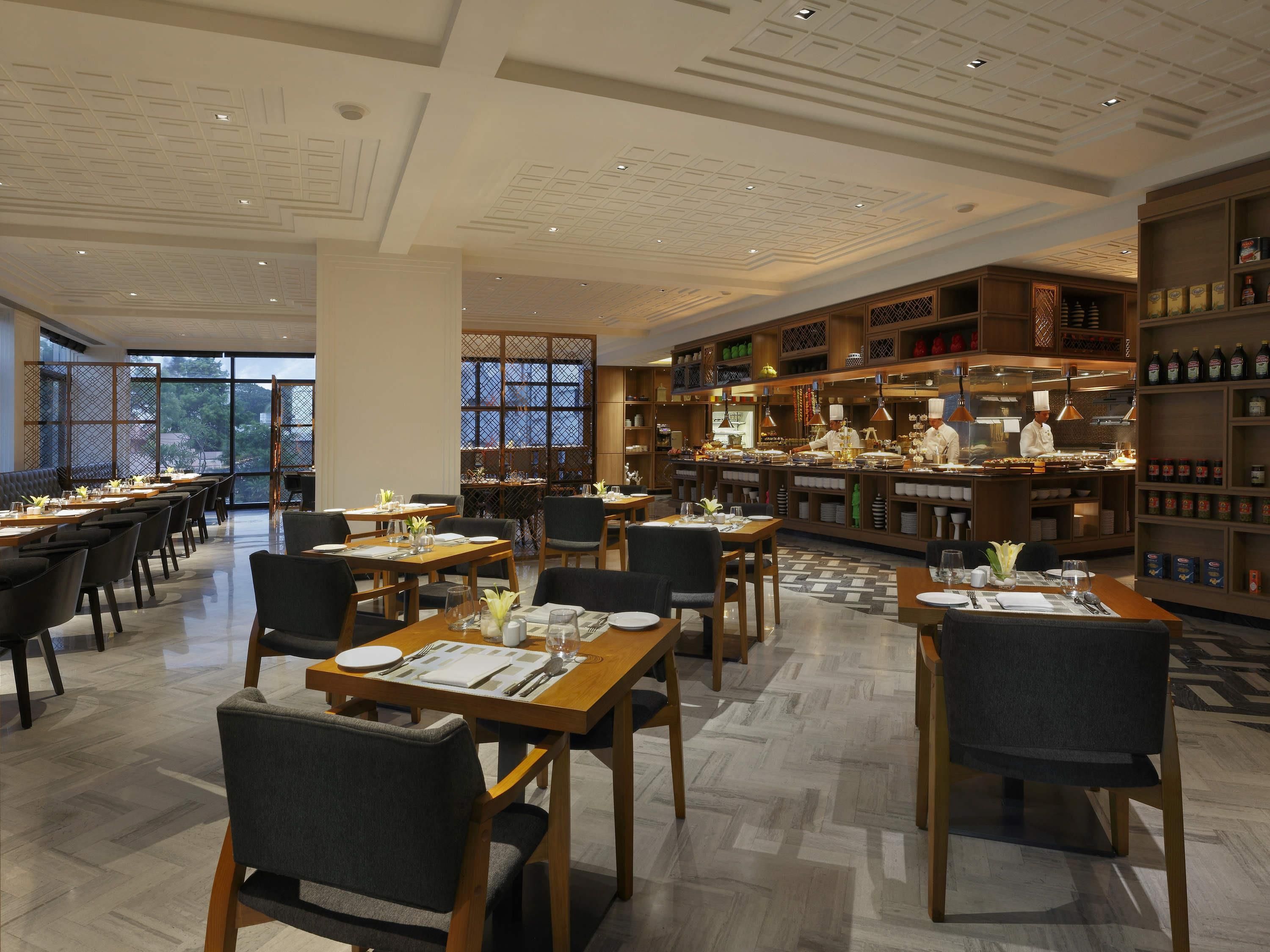 Interior moderno de restaurante com mesas, cadeiras e área de cozinha de madeira.