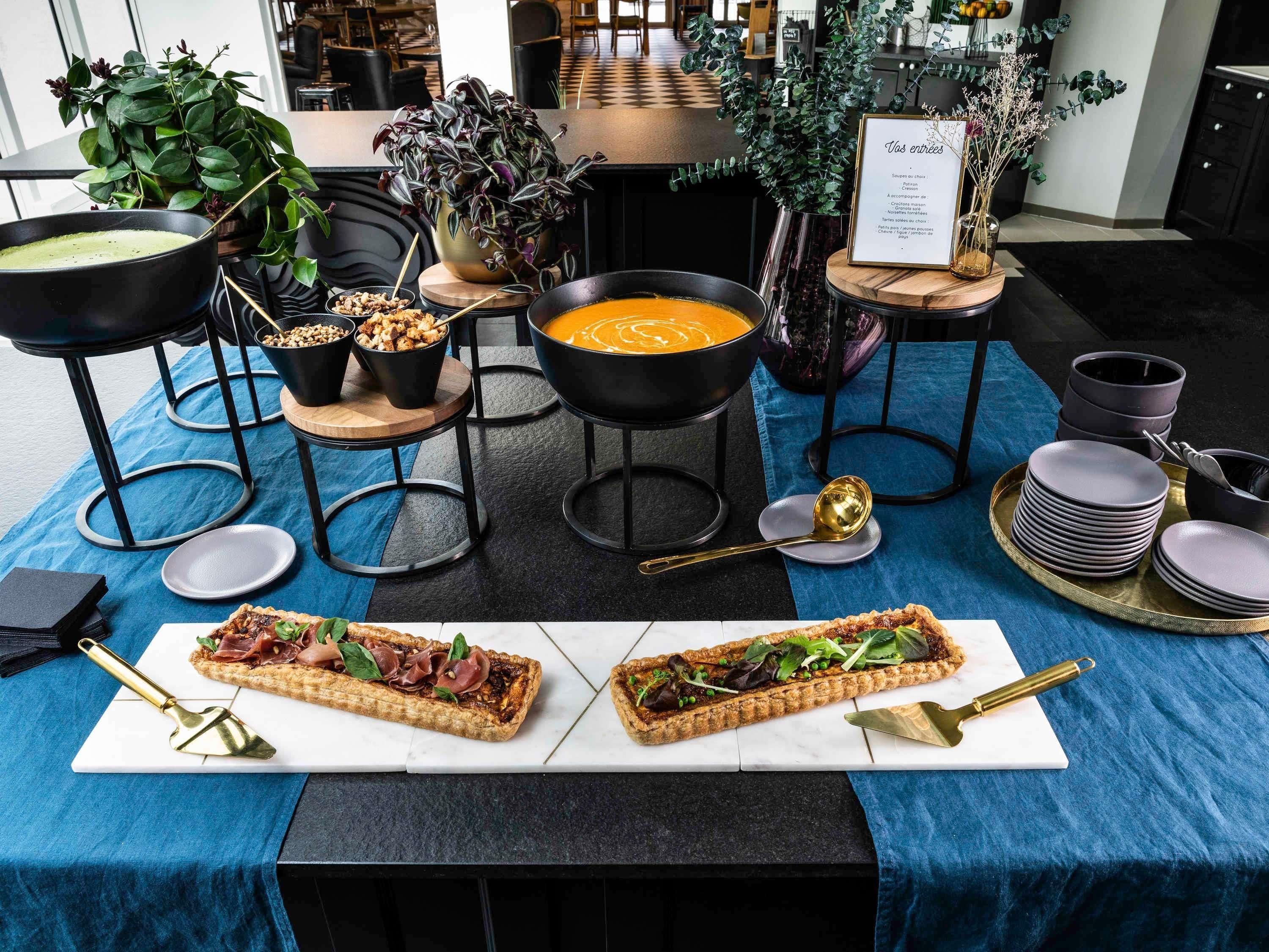 A dining area with a table set for two, featuring a variety of dishes, including a soup and a tart, and a menu sign.