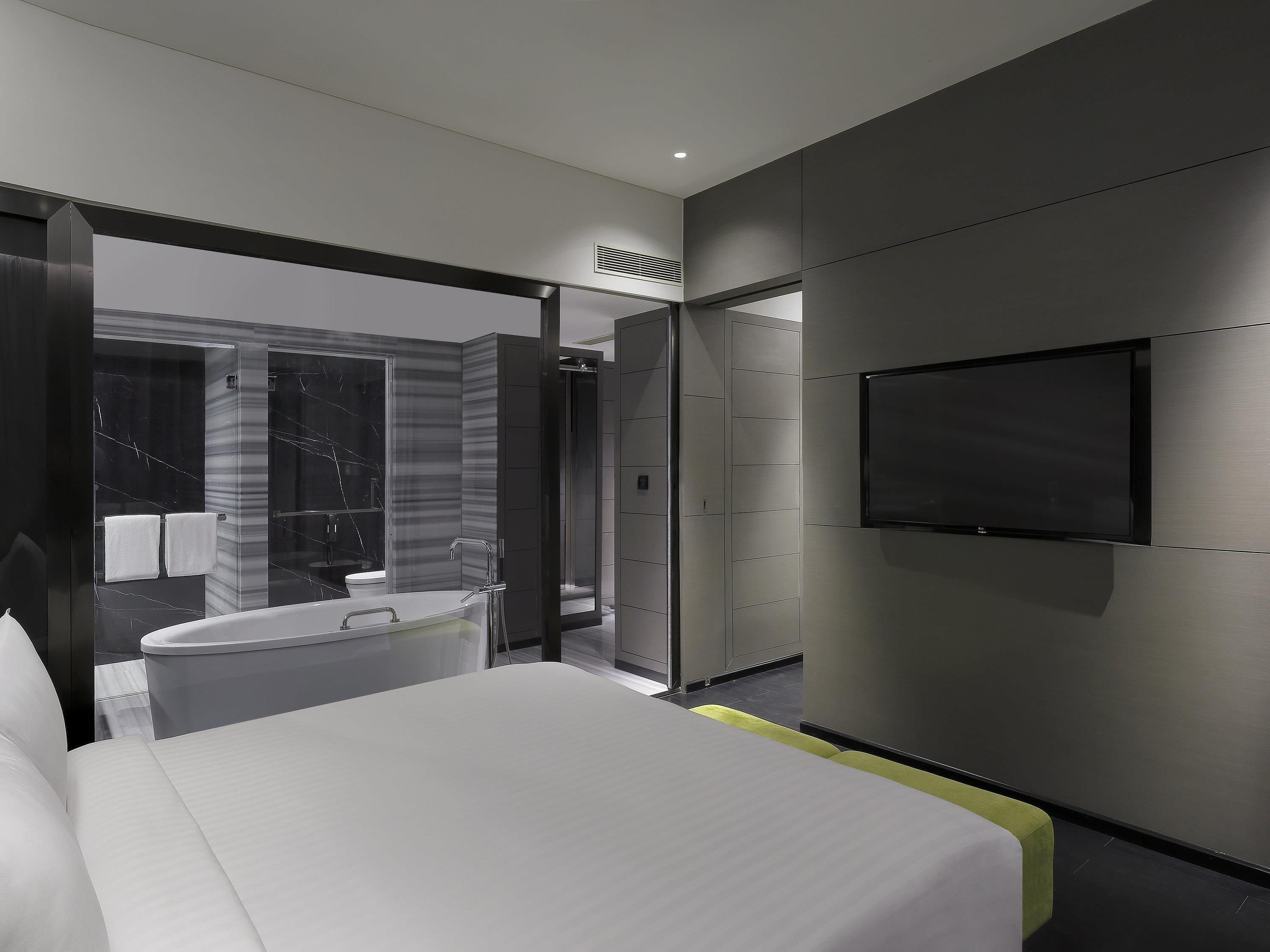 Ett modernt hotellrum med en stor säng, en TV som är monterad på väggen och ett badrum med badkar och dusch.