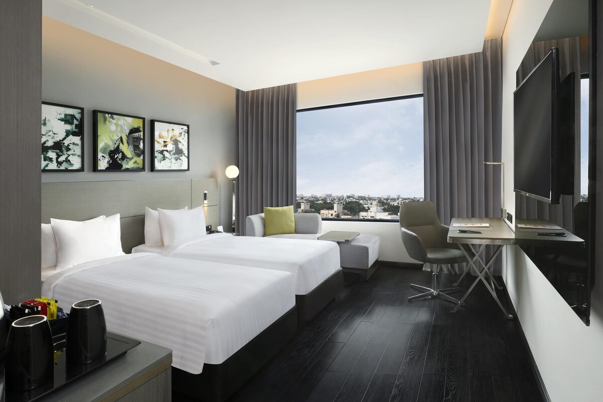 A hotel room with a large bed, a desk, a chair, a TV, and artwork on the wall.
