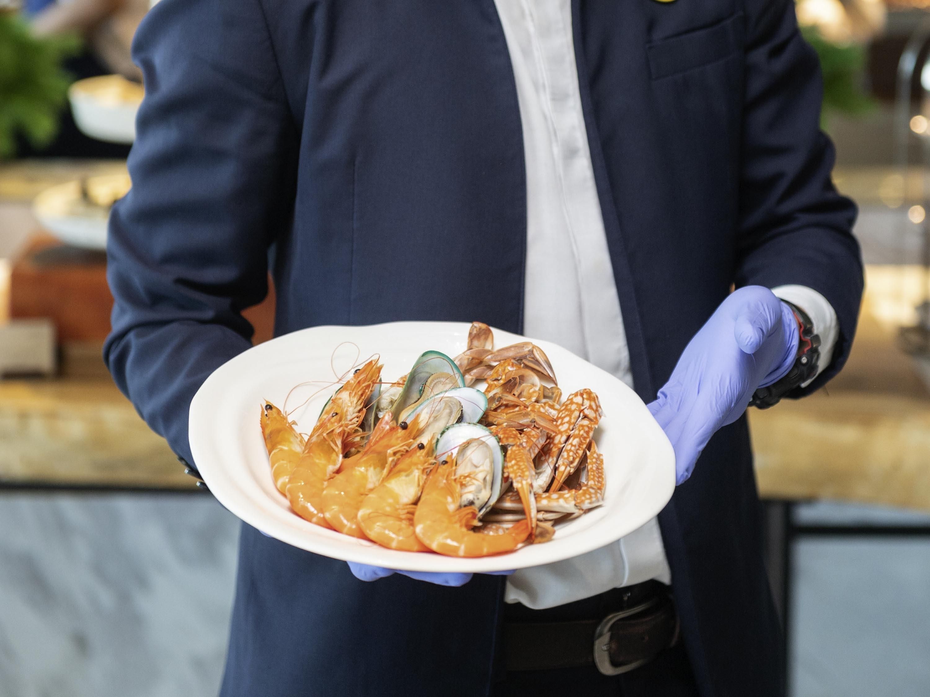 A person holding a plate with seafood, wearing a uniform and gloves.