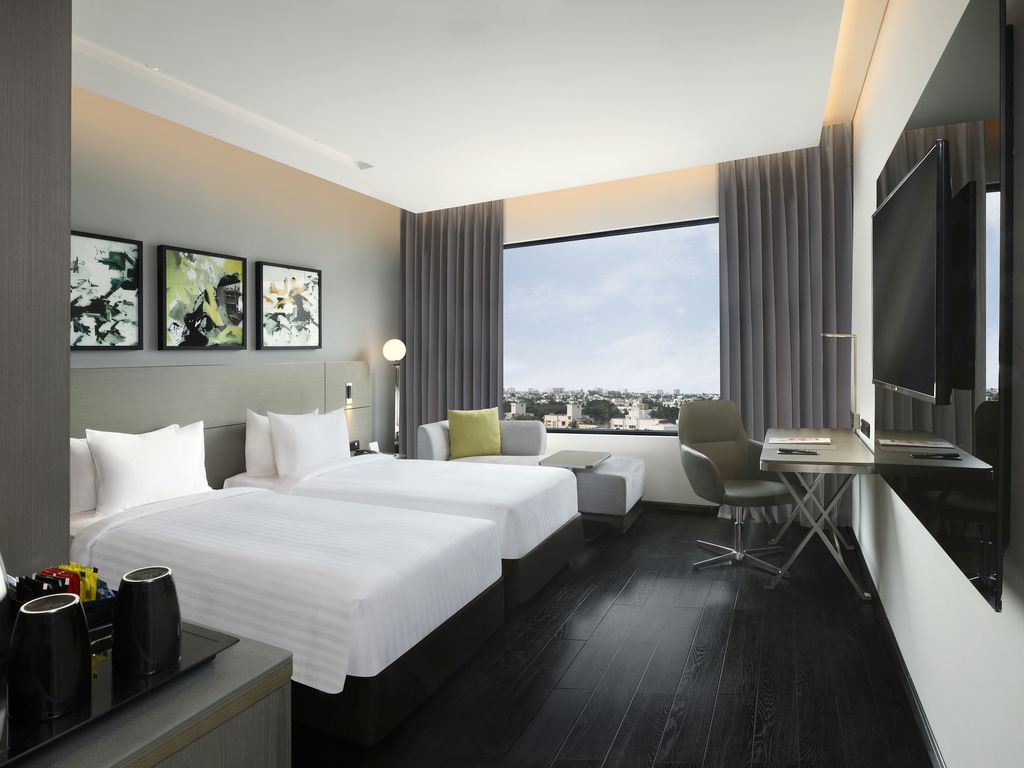 A hotel room with two beds, a desk, a chair, a TV, and a city view.