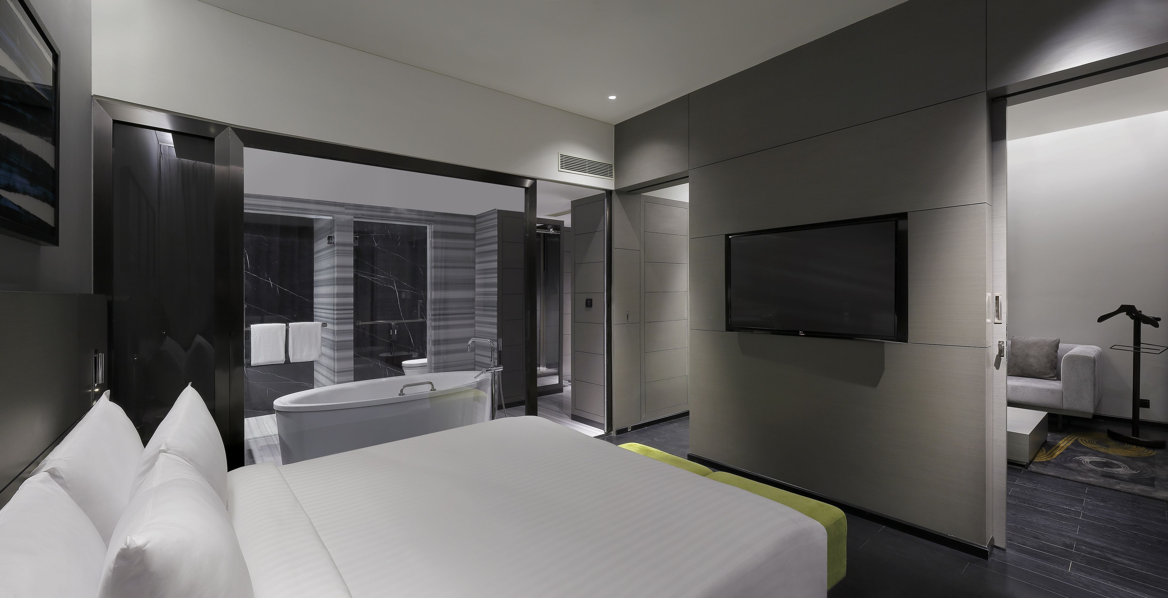 A modern hotel room with a large bed, a bathtub, a TV, and a sofa.