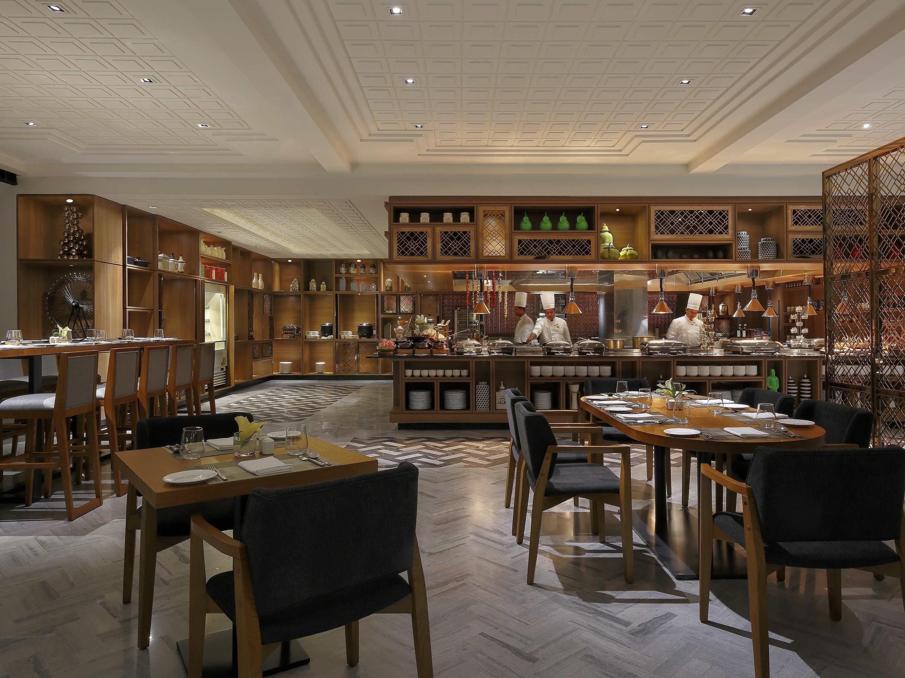 A restaurant with a central kitchen, wooden furniture, and a patterned floor.