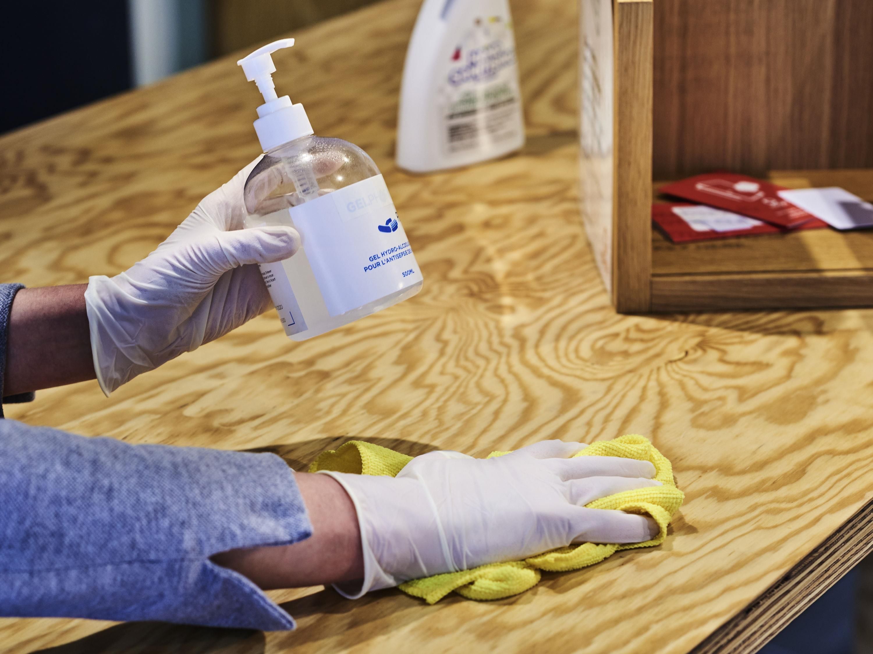 A person cleaning a wooden surface with a yellow cloth and a bottle of cleaning solution.