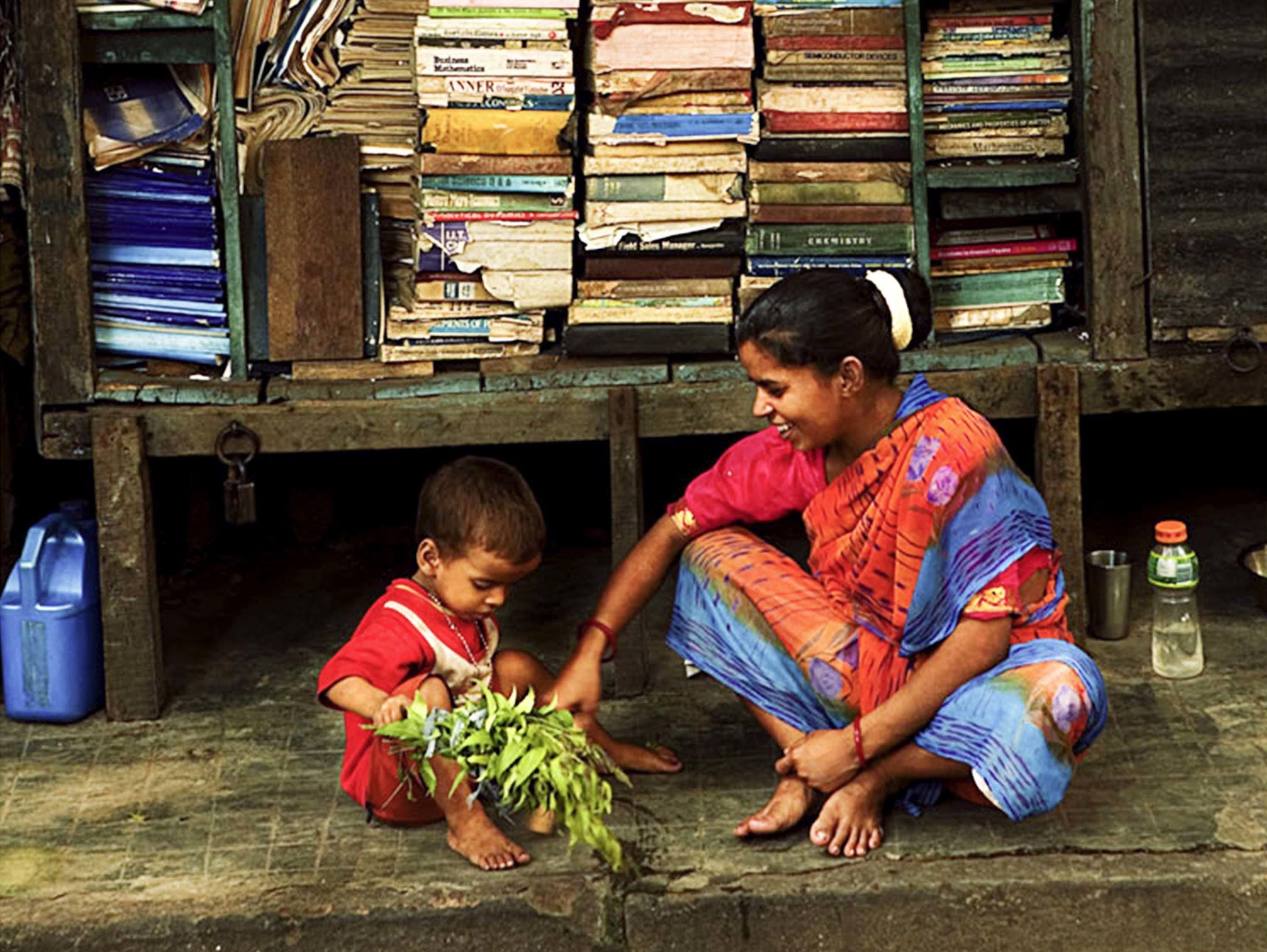 A person sitting on the ground next to a stack of books.
