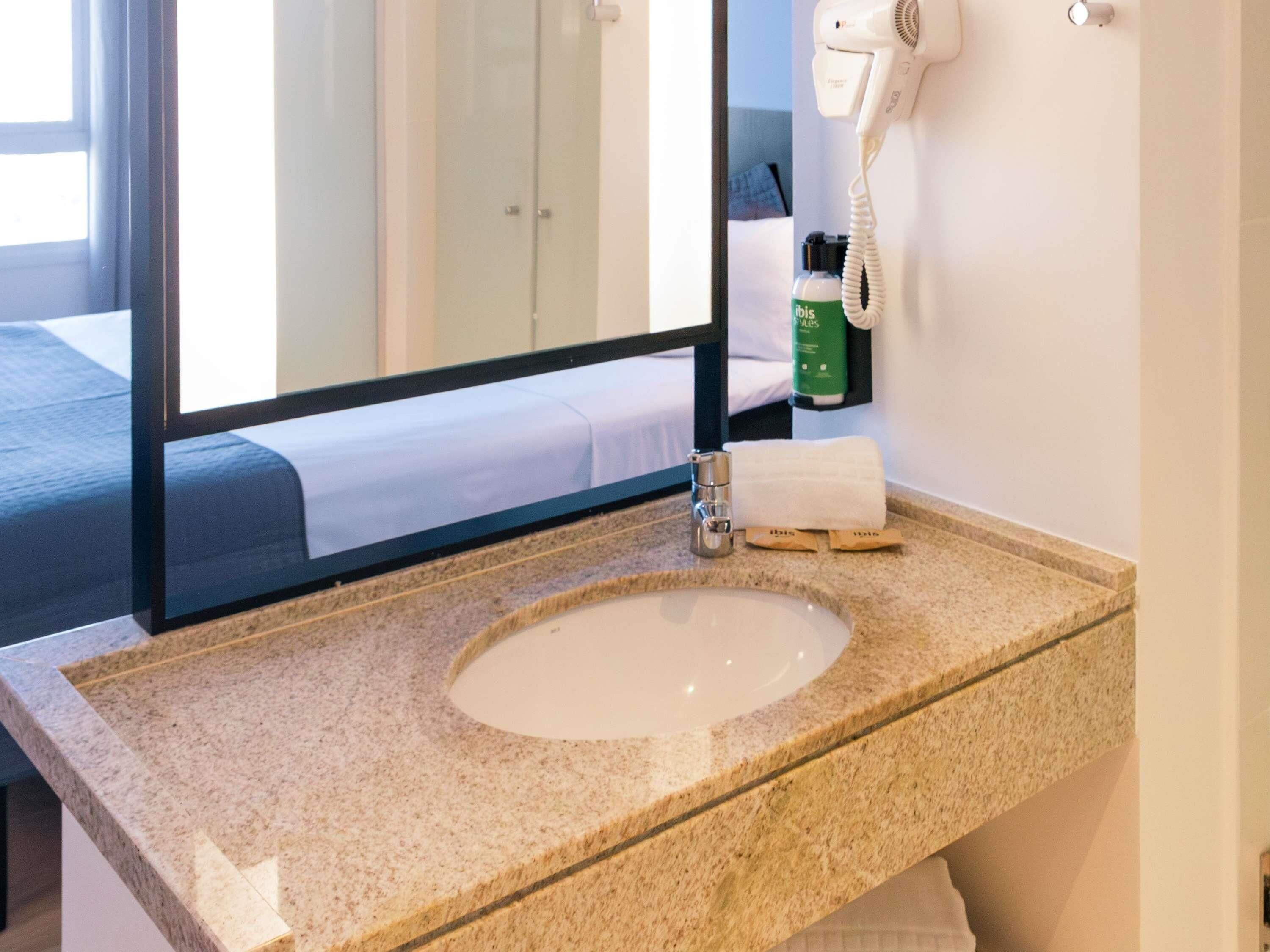 Un baño de hotel con encimera de granito, lavabo, secador de pelo y artículos de aseo.