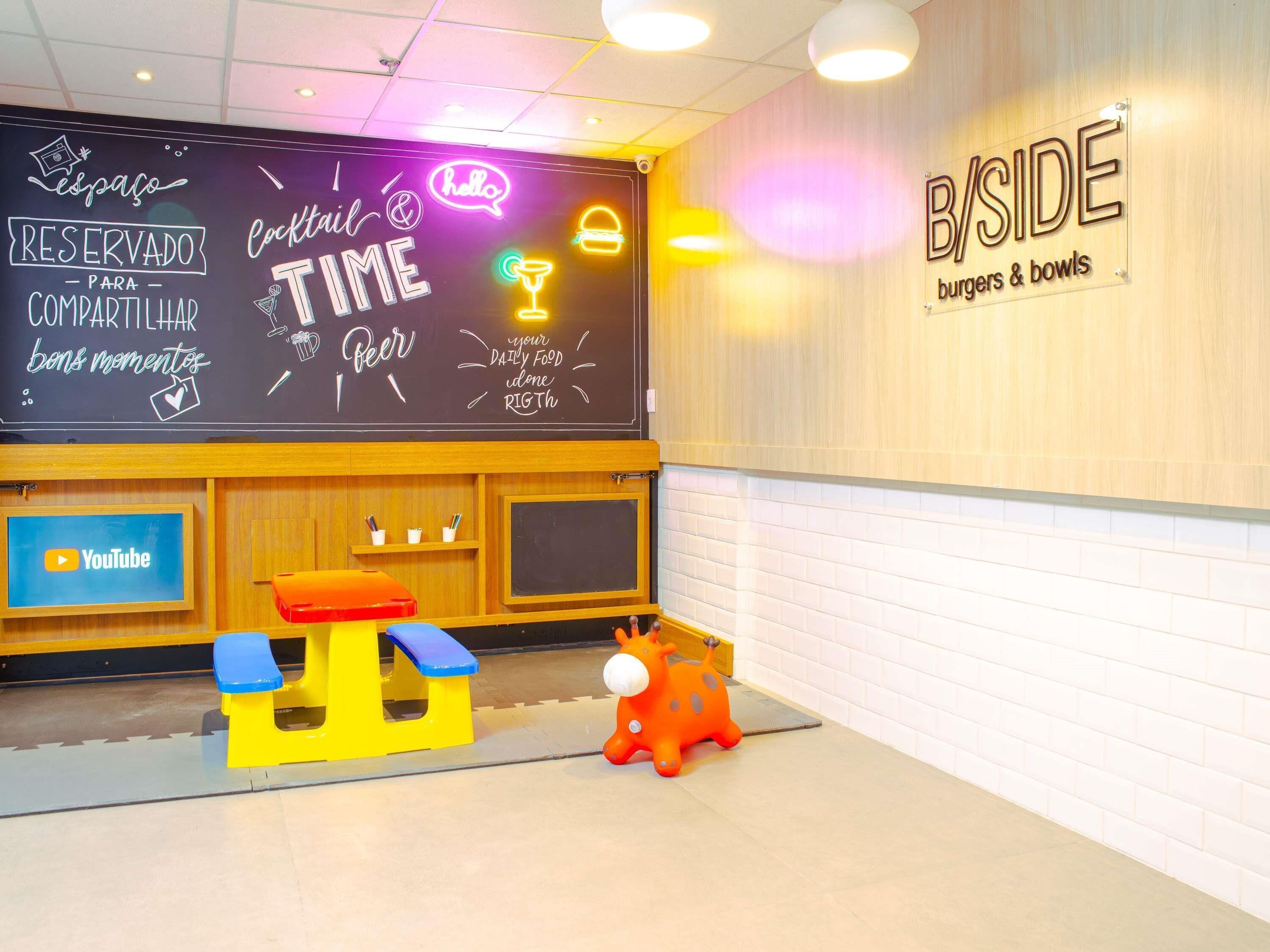 A restaurant interior with a chalkboard menu, a YouTube screen, and a playful giraffe decoration.