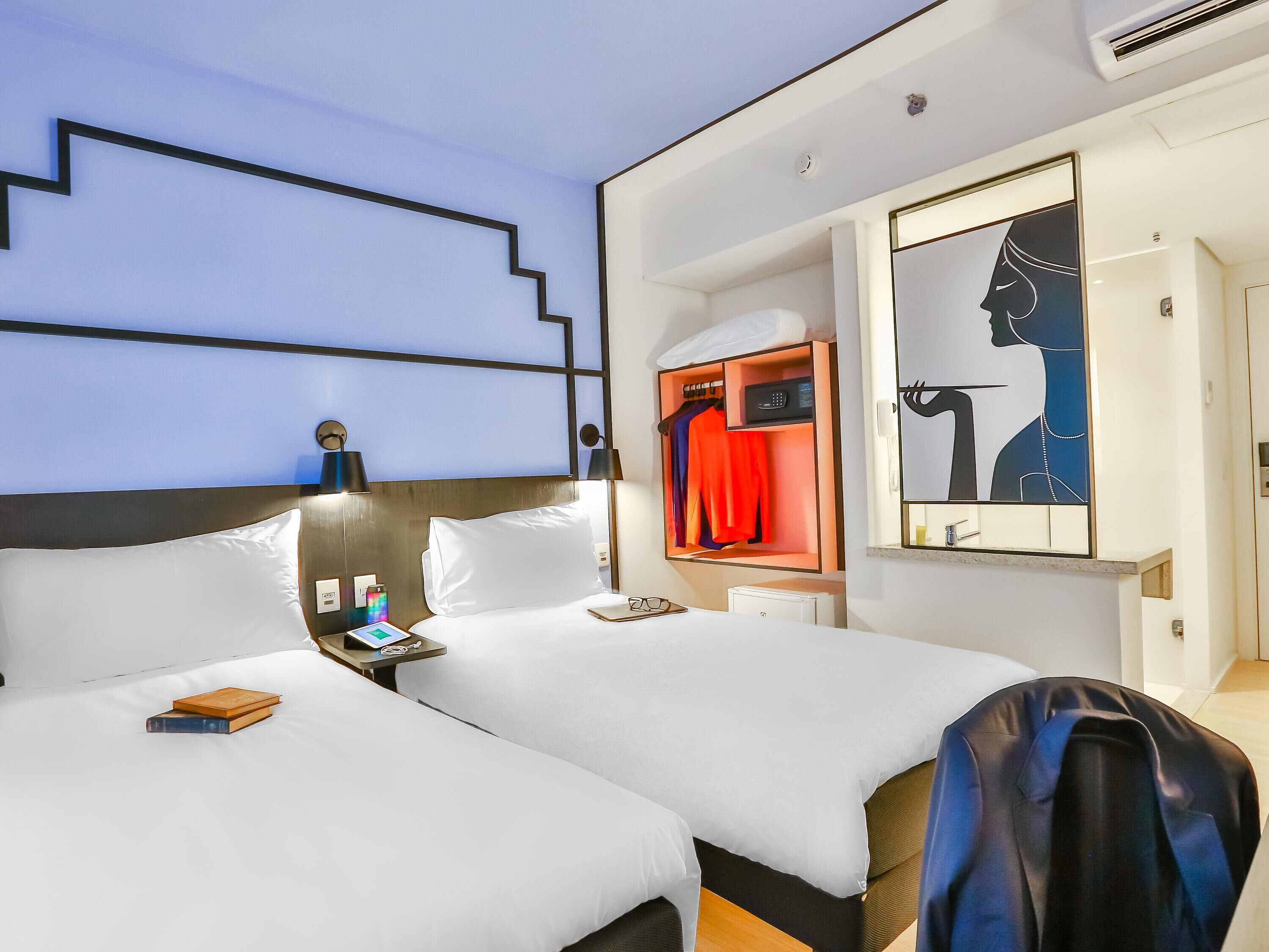 A hotel room with two beds, a wardrobe, a mirror, and a nightstand.