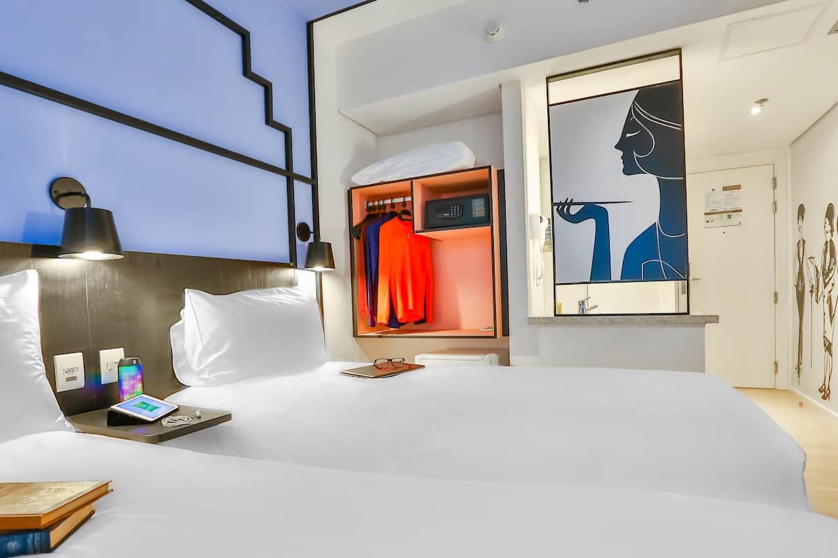 Een moderne hotelkamer met een opgemaakt bed, een nachtkastje met een lamp, een digitale klok en een nachtkastje met een boek.