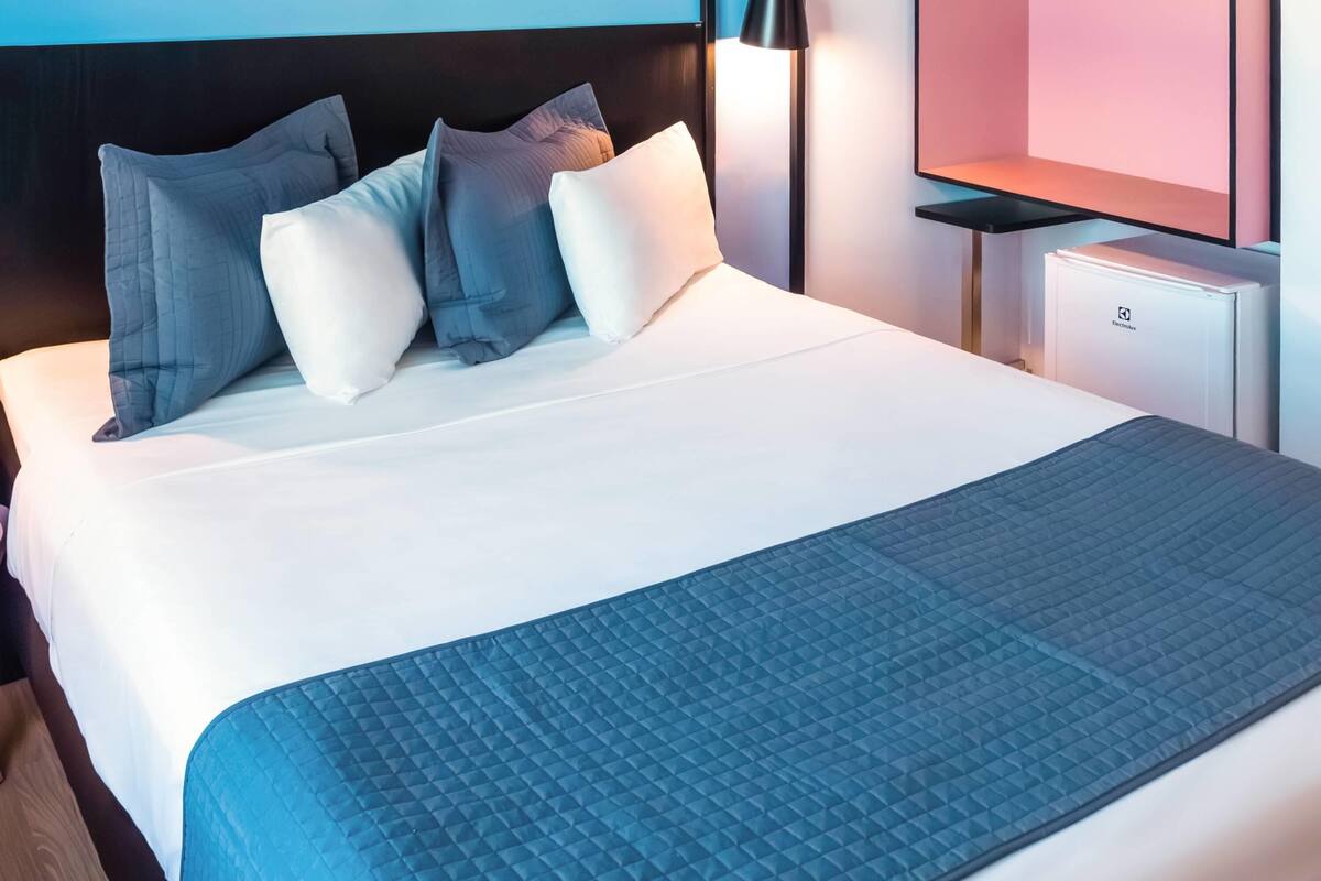 Een opgemaakt bed met een blauwe deken, witte kussens en een zwart hoofdbord.