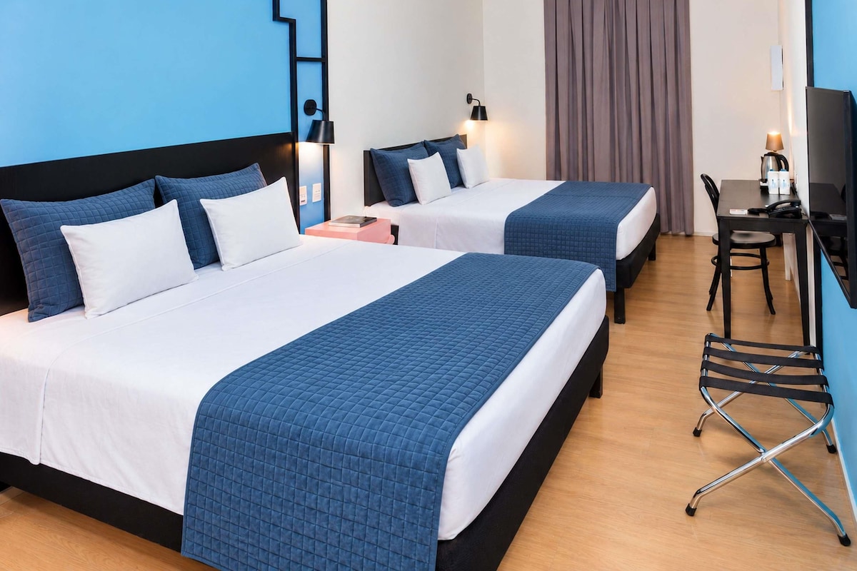A hotel room with two beds, a desk, a chair, and a television.