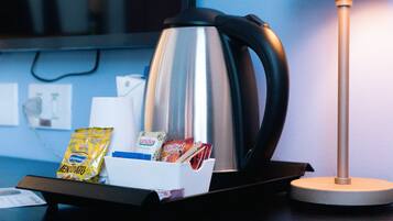 Una cafetera, una lámpara y un recipiente con provisiones sobre una mesa en una habitación de hotel.