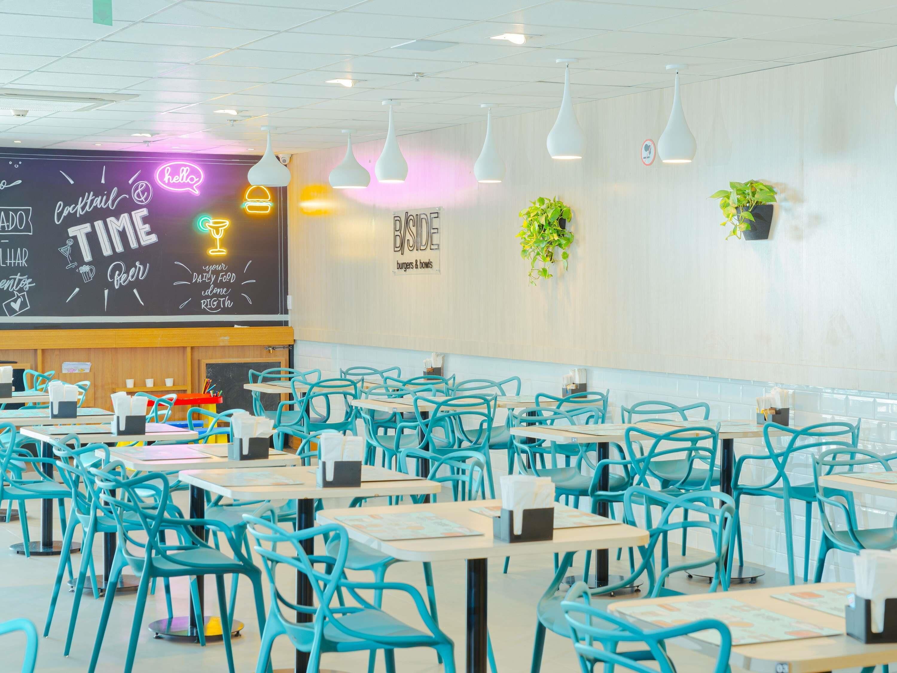 Un interior de restaurante con sillas color turquesa, mesas blancas y un menú en una pizarra.