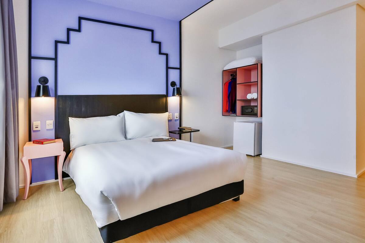 Een moderne hotelkamer met een bed, nachtkastjes, een dressoir, een spiegel en een inbouwkast.