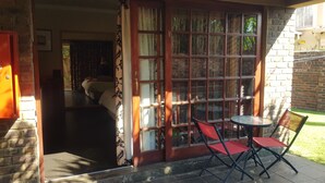 A room with a bed, a window with curtains, a table with chairs, and a door leading to another room. - La Picasso Guesthouse (Ermelo)