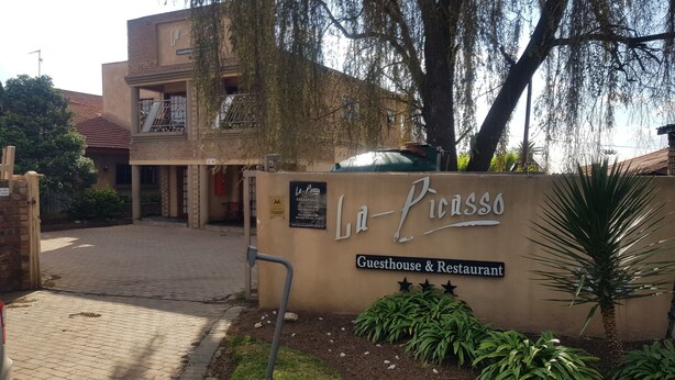 A guesthouse and restaurant named La-Picasso with a paved entrance, a signboard, and some greenery. - La Picasso Guesthouse (Ermelo)