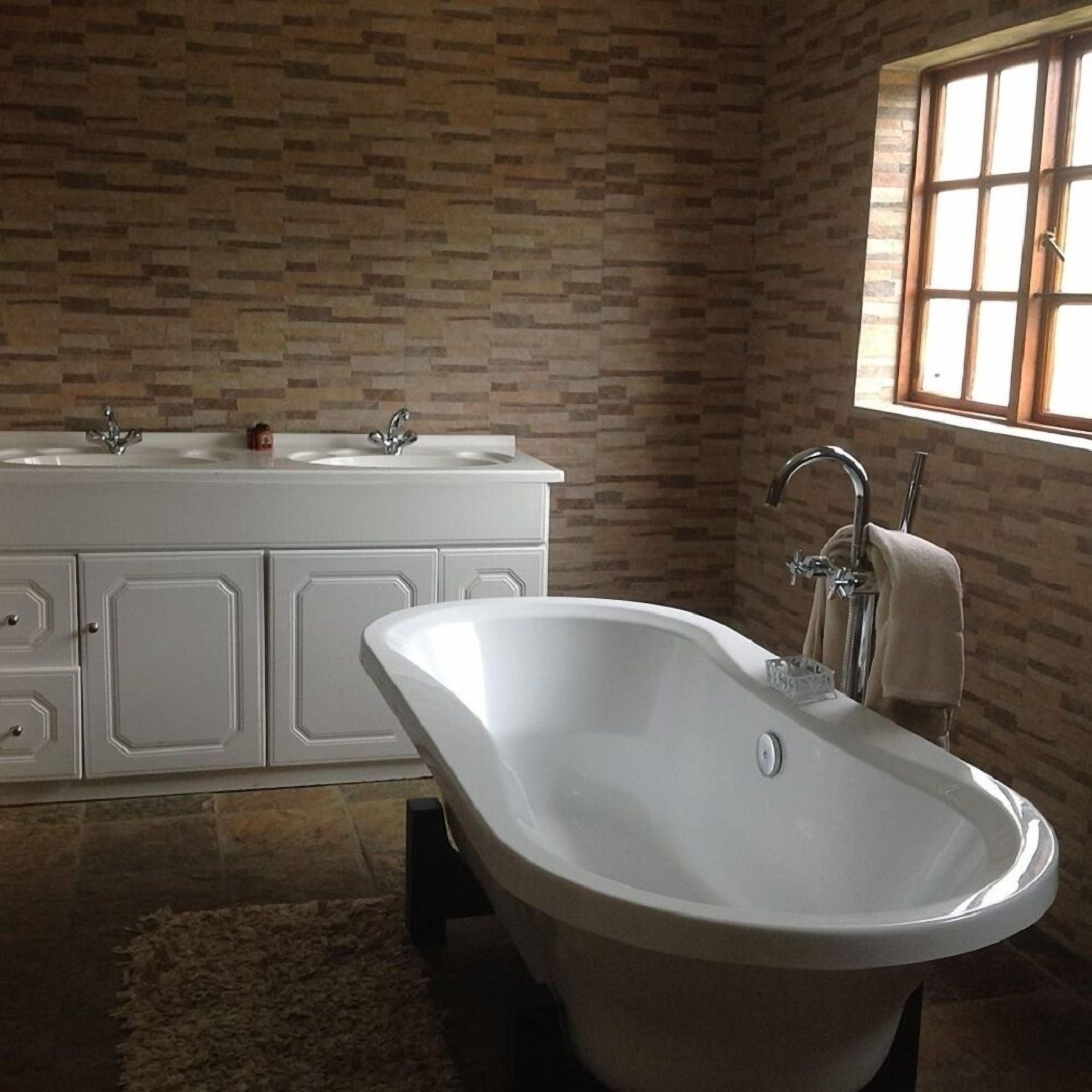 A bathroom with a freestanding bathtub, a double sink vanity, and a window with a view.