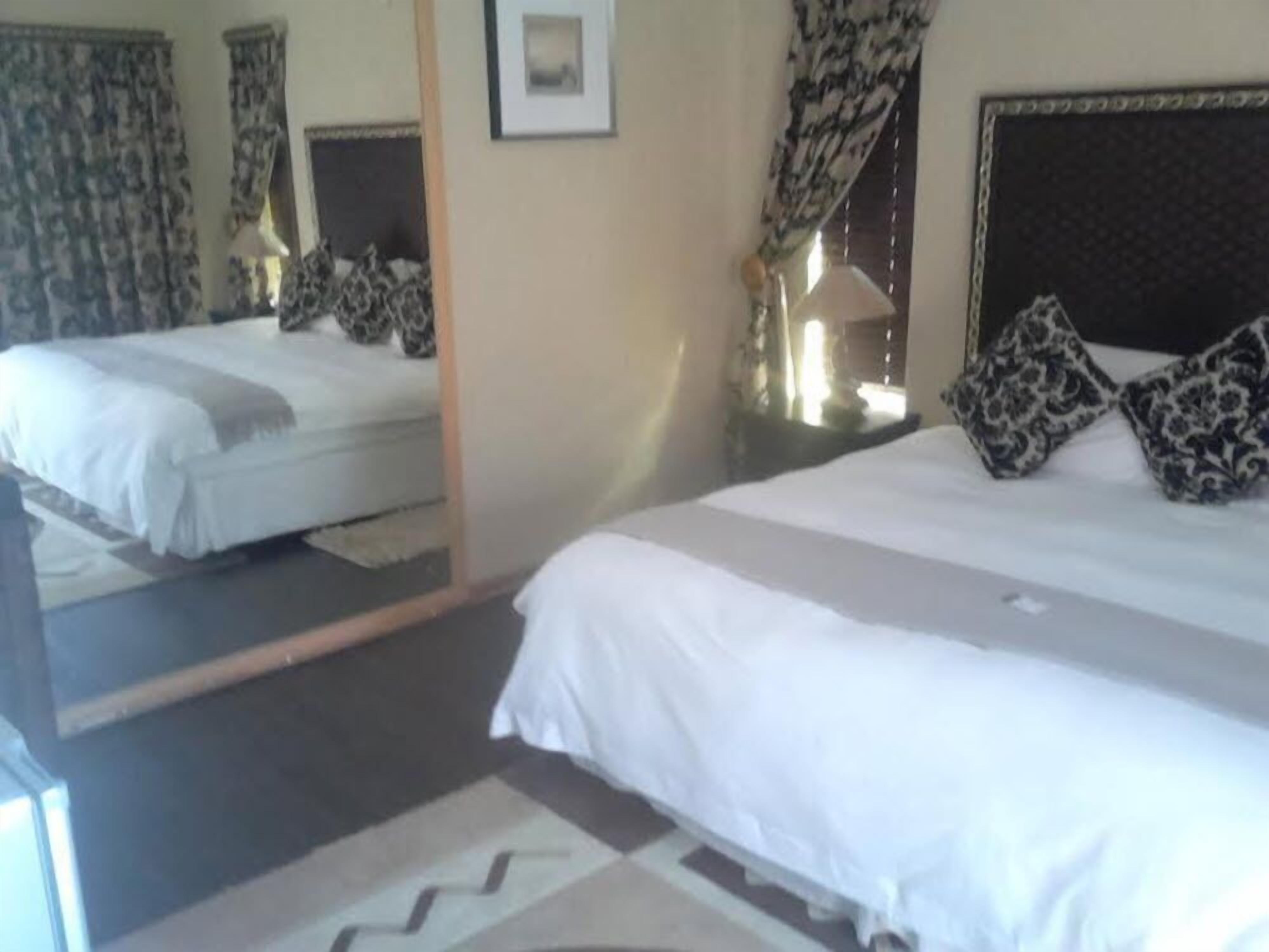 Ein Hotelzimmer mit zwei Betten, einem Spiegel, einer Lampe und gemusterten Vorhängen.