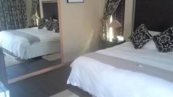 Ein Hotelzimmer mit zwei Betten, einem Spiegel, einer Lampe und gemusterten Vorhängen.