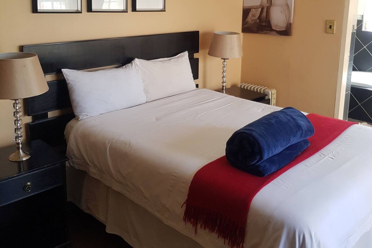 A hotel room with a bed, two bedside tables, a nightstand, and a wall with three framed pictures.