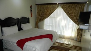 A neatly made bed with white linens and a red throw blanket, a television on a stand to the right, and a window with curtains. - La Picasso Guesthouse (Ermelo)