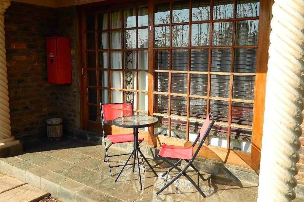 A patio with a table and two chairs, a red cabinet, and a window with blinds.