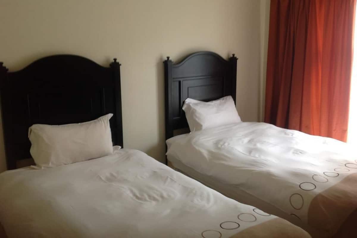 Two single beds with dark wooden headboards in a room with plain walls and a red curtain.