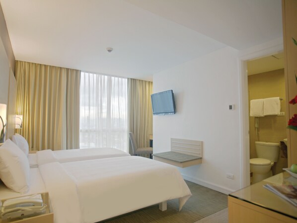 A hotel room with two beds, a TV, a desk, and a bathroom. - St Giles Makati (Makati)
