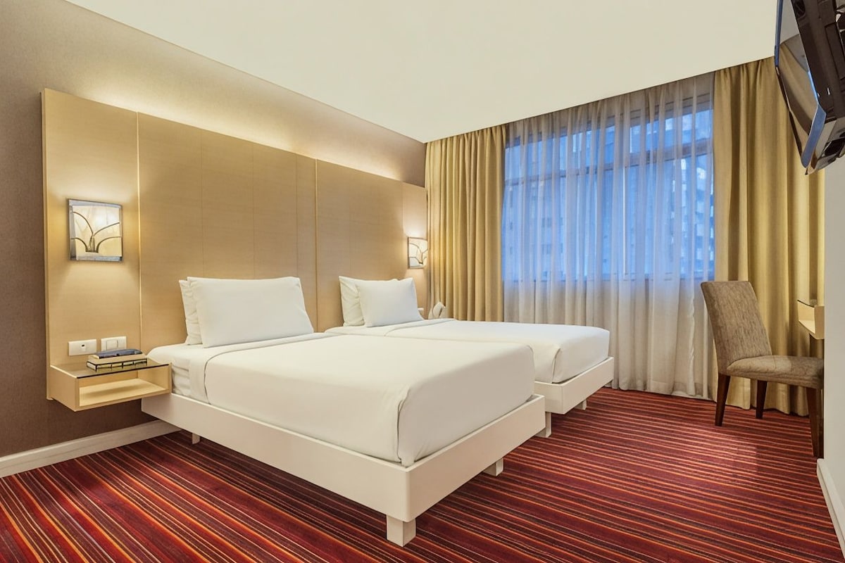 Een hotelkamer met twee bedden, een televisie, een nachtkastje en een stoel.