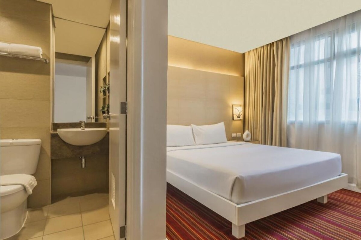 Een hotelkamer met een bed, een badkamer met een wastafel en een raam met gordijnen.