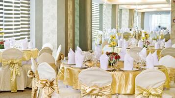 Une salle de banquet avec des tables rondes dressées pour un événement formel, agrémentée de nappes dorées et blanches, de chaises ornées de rubans dorés et de compositions florales en guise de centre de table.