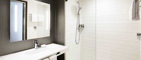 A modern bathroom with a glass-enclosed shower, a white sink, and a large mirror.