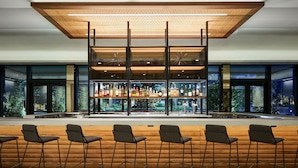 A bar area with a wooden counter, multiple shelves of bottles, and bar stools. - AC Hotel by Marriott Tampa Airport (Tampa)