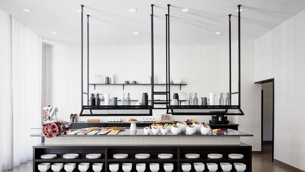A modern kitchen with a central island, black shelving, and a variety of kitchenware. - AC Hotel by Marriott Tampa Airport (Tampa)