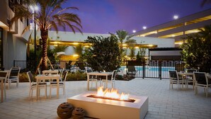 An outdoor patio area with a rectangular fire feature, seating arrangements, and a pool in the background. - AC Hotel by Marriott Tampa Airport (Tampa)